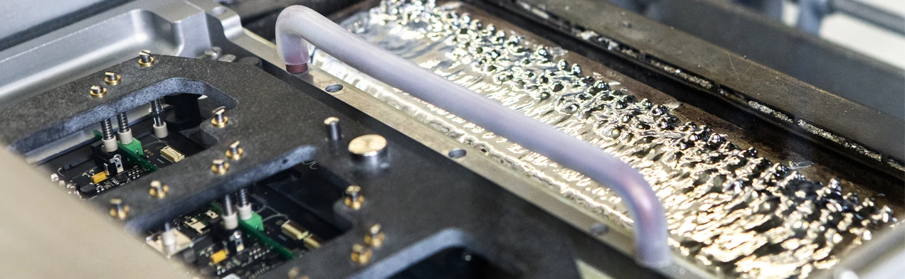 This image shows a solder frame dipping into a wave of liquid solder in a wave soldering machine, typical for THT manufacturing processes at Cloos Electronic. It illustrates the precise application of soldering technology for the production of high-quality electronic boards.