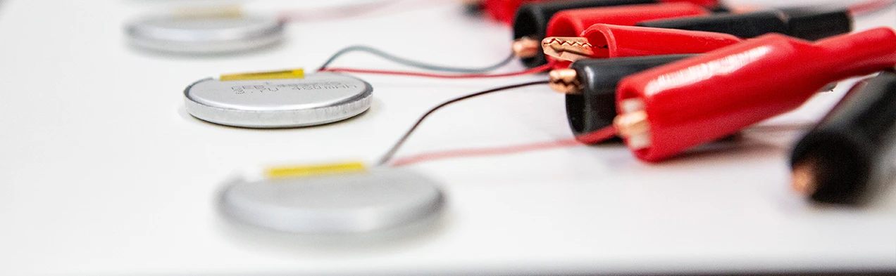 This image shows small round LiPo batteries connected to a battery tester, demonstrating Cloos Electronic's expertise in battery sourcing. It highlights the ability to test and provide high-quality batteries for various applications.
