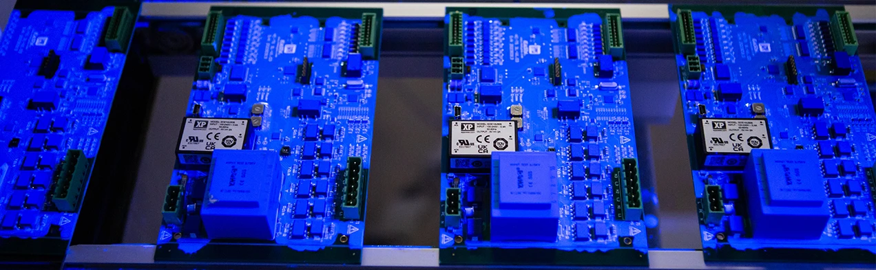 This image shows electronic cards passing under UV light on a conveyor belt as part of the automated conformal coating process at Cloos Electronic. This technique protects sensitive components and enhances product durability.