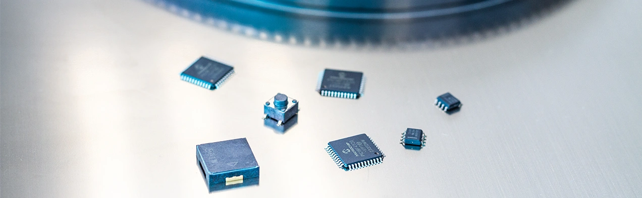 This image displays integrated circuits (ICs) and electronic components arranged in front of a component reel, representing the sales of these components by Cloos Electronic. It highlights the electronic parts available.